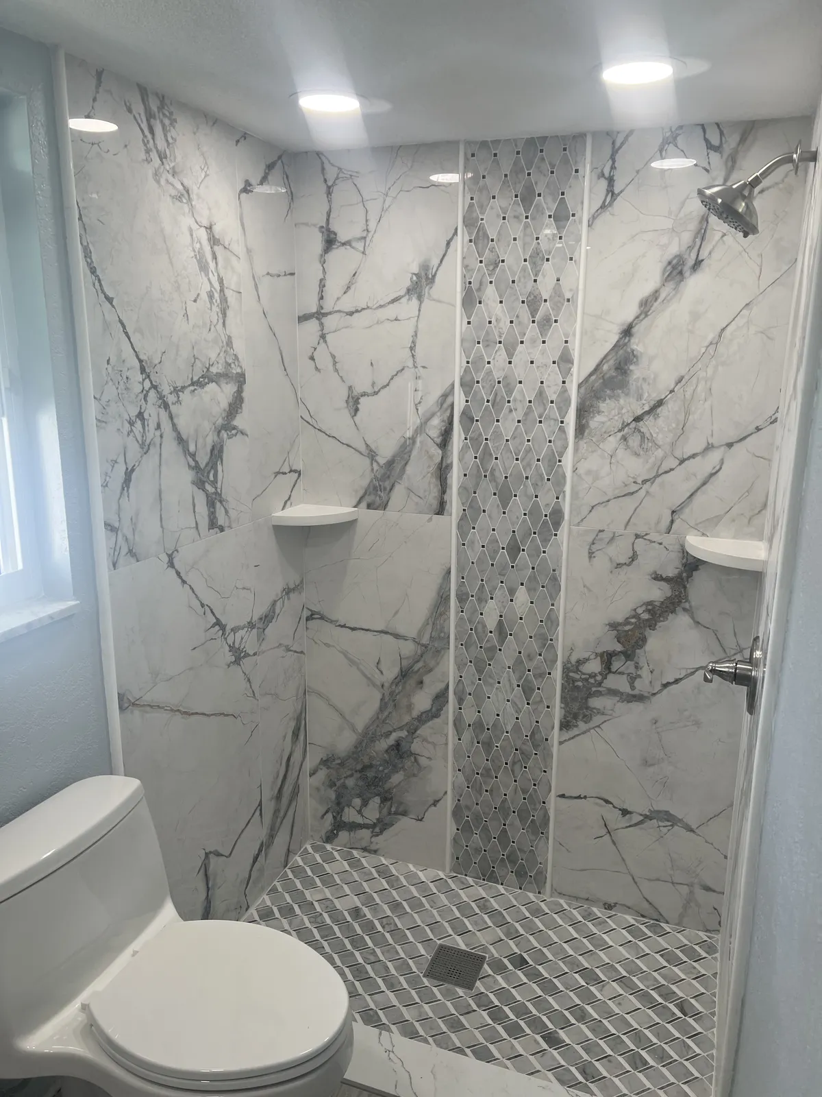 Coastal Lane luxury bathroom finish — book-matched marble slab walk-in shower with a diamond mosaic inlay